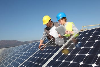 A man and a women in hard hats are inspecting solar panels