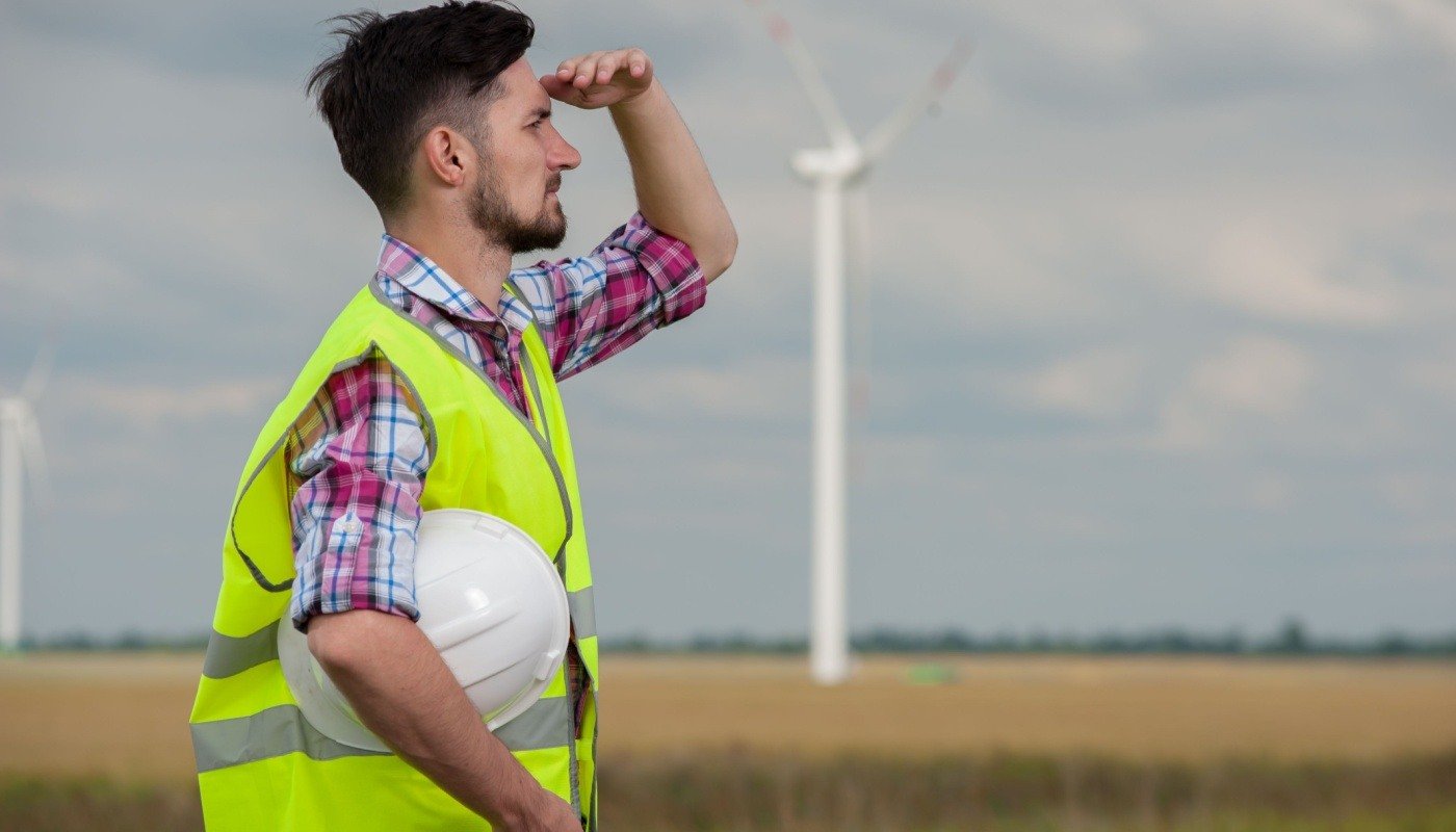 Man with hand on forehead looking out in a wind turbine field